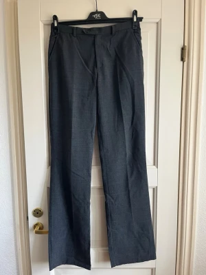 Mörkgrå kostymbyxor från Filippa K - Mörkgrå kostymbyxor med rak passform och pressveck. Modellen har bälteshällor, sidofickor samt två dekorativa bakfickor. Byxbenen är uppsprättade för extra längd – jag är 175 cm lång och de sitter perfekt på mig.