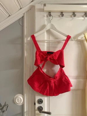 Röd linnetopp med rosett från Zara - Snygg röd/korall linnetopp från Zara med breda axelband och stor rosettdetalj framtill. Toppen har en öppen detalj under bysten och är croppad i modellen. Perfekt för varma dagar och ger en trendig look.