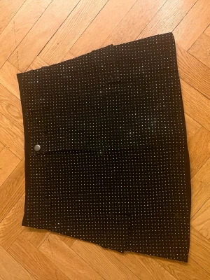 Svart kortkjol med vita prickar - Säljer en svart jean kortkjol med små rhinestones i ett prickigt mönster. Kjolen har en rak passform och en knappdetalj framtill. Perfekt för dig som gillar en enkel men ändå lekfull stil.Skriv gärna för mått! 💕