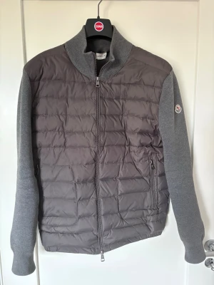  Moncler cardigan grå - Säljer min Moncler cardigan i storlek L men passar som en M. En söm har börjat gå upp lite som ni ser på 3de bilden annars inga defekter. Ägt den i ungefär 1 år kvitto saknas. Säljer pga för kort i längd för mig. Min längd är 183 och väger 68kg tveka ej att skriva vid intresse och kom med bud :)