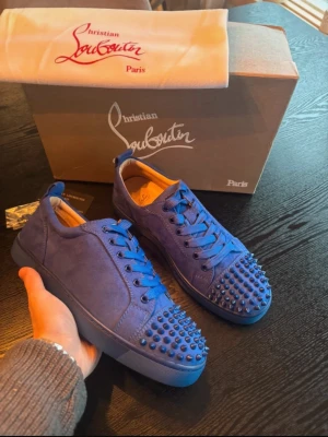 Christian Louboutin skor blå - Säljer ett par blå sneakers från Christian Louboutin i mocka med matchande blå nitar på tån. Perfekta skor nu i sommar om du vill sticka ut med en unik och nichig stil. Dom är knappt använda och har inga effekter. Storleken är 40 men dom har större passform runt 41. Hör av dig vid frågor och tveka inte på att slänga iväg ett prisförslag!
