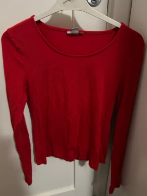 Röd långärmad topp från NewYorker - En enkel och snygg röd långärmad topp från NewYorker. Modellen har rund halsringning och är tillverkad i ett mjukt material som sitter skönt på kroppen. Perfekt att matcha med jeans eller kjol för en clean look. Tröjan är i storlek S.