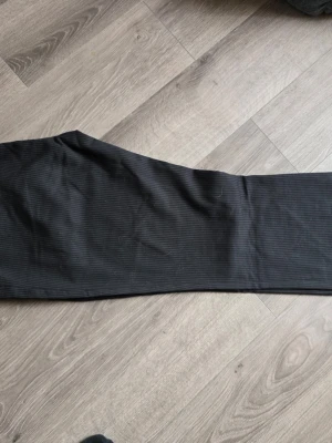 Svarta kritstrecksrandiga byxor från HM - Säljer ett par svarta byxor med diskreta kritstrecksränder. Byxorna har raka ben och är tillverkade i ett mjukt material som ger en bekväm passform. Perfekta för dig som gillar en enkel och stilren look. Storlek 42