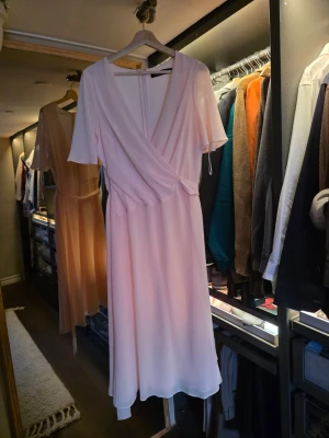 Lauren Ralph Lauren Ljusrosa omlottklänning med knyt - Säljer en ljusrosa omlottklänning med knyt i midjan och korta, fladdriga ärmar. Klänningen har en mjuk, flowy passform och är tillverkad i ett tunt, skönt material som passar perfekt till sommaren. Enkel men elegant design som ger en romantisk känsla. Strl 42 (10). Skickar snabbt!  Använd en gång.