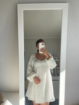 Vit spetsklänning med puffärmar - Söt vit kortklänning med romantisk spets och puffiga långa ärmar. Klänningen har omlottkänsla vid bysten och kan bäras både på axlarna och offshoulder. Perfekt för sommarens tillfällen och har en luftig passform.