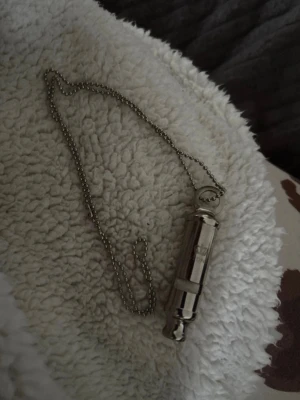 Metallvisselpipa på kedja - Snygg visselpipa i silverfärgad metall med tillhörande kulkedja. Perfekt som accessoar för dig som vill sticka ut eller ha något unikt runt halsen. Klassisk cylinderform och stilren design.
