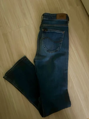 Mörkblå jeans från Lee 28/31 - Snygga mörkblå jeans från Lee med klassisk femficksdesign och raka ben. Jeansen har en läderpatch med Lee-logga bak i midjan och är tillverkade i slitstark denim. Perfekta för en avslappnad och trendig look.