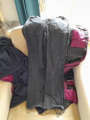 Svarta bootcut jeans med rå kant - Säljer ett par svarta bootcut jeans med rå, fransig kant nertill. Jeansen har klassisk femficksdesign och en något utsvängd passform. Perfekta för en avslappnad och trendig look.