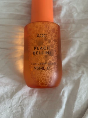 AOC Peach Bellini Hair & Body Mist - Fräsch och fruktig Peach Bellini hair & body mist från AOC. Flaskan är orange med frostad finish och rymmer 95 ml. Perfekt för dig som gillar dofter med inslag av persika och vill ha en lätt mist för både hår och kropp.