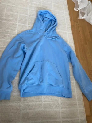 Ljusblå hoodie med magficka - Snygg ljusblå hoodie med klassisk huva och dragsko. Hoodien har en stor magficka framtill och ribbade muddar vid ärmslut och nederkant. Perfekt för en avslappnad och chill stil. Materialet känns mjukt och bekvämt, troligen bomull eller bomullsblandning.