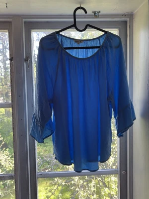 Blå blus  - Snygg blå blus  med rund halsringning och vida, långa ärmar. Perfekt för en trendig och luftig look. Enkel att matcha med både jeans och kjol. Färgen är baby blå vilket passar perfekt till sommaren!