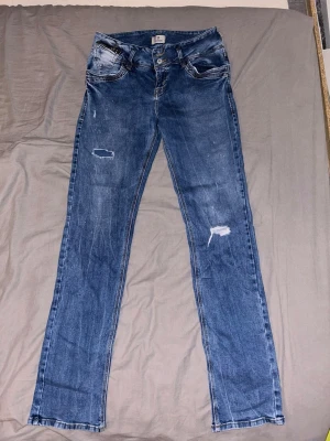 Low waist jeans - Säljer ett par blå jeans från LTB med raka ben/utsvänga och slitna detaljer på låren och knäna.  32/34