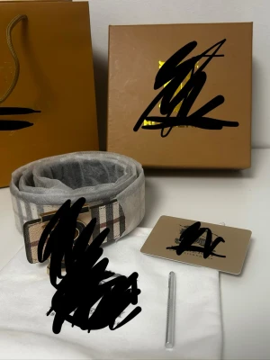 Rutig skärp med gulddetaljer - Snyggt skärp med klassiskt rutigt mönster i beige, svart och brunt. Spännet är i guld och ger en lyxig känsla. Perfekt accessoar för att lyfta vilken outfit som helst.