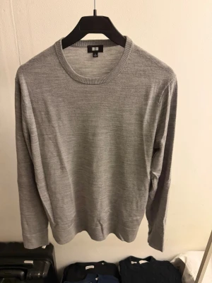 Merino ull tröja  - Snygg och enkel grå stickad tröja från Uniqlo i tunt material. Tröjan har rund halsringning, långa ärmar och en klassisk passform som funkar till det mesta. Perfekt basplagg för lager på lager och stilrena outfits.