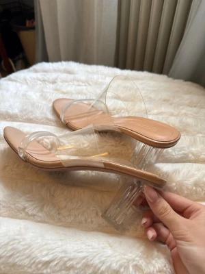 Transparenta pumps med klack från Fashion - Säljer ett par trendiga pumps med transparent rem och klar blockklack. Skon har en nude-färgad innersula och öppen tå. Perfekt för dig som gillar en modern och stilren look. Materialet är plast och syntet. Kolla sista bilden för att se att plasten är något smutsig, men det syns bara om man kollar noga skulle jag säga. (Skokartong medföljer) 
