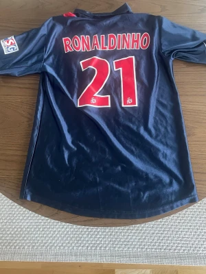 PSG fotbollströja Ronaldinho #21 - Klassisk PSG matchtröja från Nike med Ronaldinho och nummer 21 på ryggen. Perfekt för fotboll eller samling.