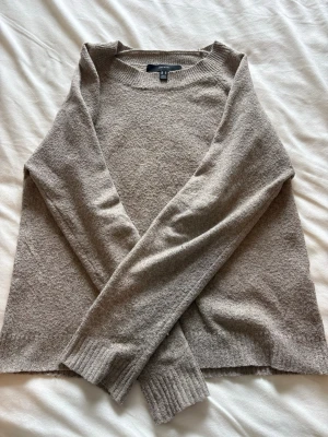Beige stickad tröja från Vero Moda - Mysig beige stickad tröja från Vero Moda med rund halsringning och långa ärmar. Tröjan har en enkel och stilren design med ribbstickade muddar vid ärmslut och nederkant. Perfekt för lager-på-lager och chill dagar.