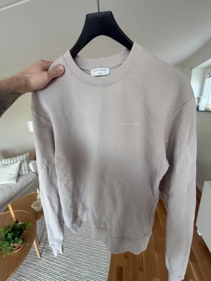 Beige sweatshirt från Tiger of Sweden - Snygg beige sweatshirt från Tiger of Sweden med diskret logga på bröstet. Tröjan har rund halsringning, långa ärmar och ribbade muddar vid ärmslut och nederkant. Perfekt för en avslappnad och stilren look.