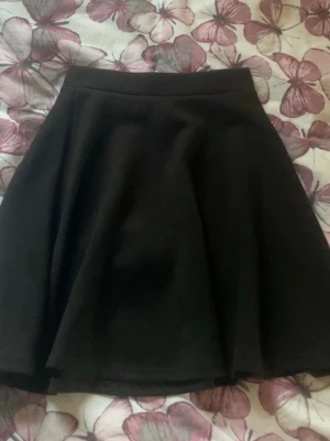 Svart kortkjol från C.W. - Enkel och snygg svart kortkjol från C.W. Kjolen har en klassisk A-linjeform och är tillverkad i en mjuk blandning av polyester och viskos. Perfekt att matcha med en crop top eller stickad tröja för en trendig look.
