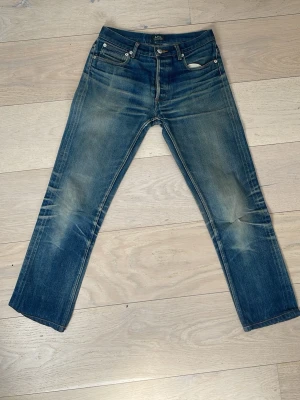 A.P.C Selvedge jeans - Säljer ett par klassiska blå jeans från A.P.C. med raka ben och snyggt slitna detaljer på framsidan och baksidan. Jeansen har fem fickor, knappgylf och är gjorda i kraftig denim. Perfekta för en avslappnad och trendig look.