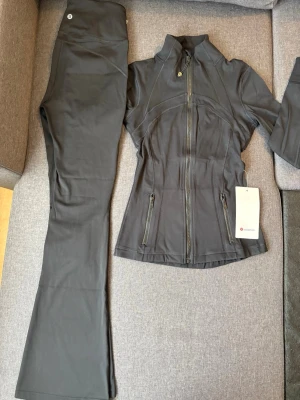 Svart träningsset från Lululemon - Snyggt svart träningsset från Lululemon med figursydd jacka och utsvängda byxor. Jackan har dragkedja, hög krage och fickor med dragkedja. Materialet är stretchigt och följsamt, perfekt för träning eller yoga. Storlek är S men passar perfekt också till XS .Priset kan diskuteras!💖🌷🌸labels are not available in the item .