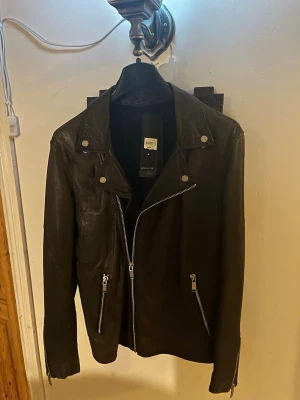 Svart skinnjacka från Filippa K - Snygg svart skinnjacka från Filippa K med klassisk bikerstil. Jackan har snedställd dragkedja, silverfärgade detaljer och dragkedjor vid ärmslut och fickor. Perfekt för dig som vill ha en stilren och tidlös look.