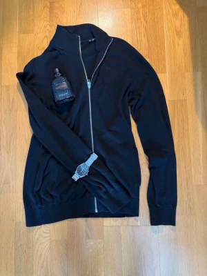 Svart ziptröja från Jack & Jones - Svart ziptröja från Jack & Jones med silverfärgad dragkedja, perfekt för en stilren och enkel look. Materialet känns mjukt och bekvämt.