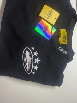 Svart hoodie från corteiz - Svart hoodie från corteiz med broderad logga och stjärnor på bröstet. Tröjan har en klassisk passform och ribbade muddar. Märkets etikett och holografisk tagg sitter kvar. Perfekt för dig som gillar streetwear och snygga detaljer.