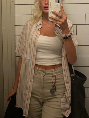 Randig skjorta - Säljer en luftig skjorta från H&M med korta ärmar och klassisk krage. Skjortan har smala ränder i beige, blått, vitt och orange samt en bröstficka. Perfekt för en avslappnad stil går att stylea på flera sätt!