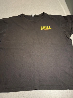 Svart t-shirt Chill Forever tryck - Svart t-shirt med gult tryck 'CHILL FOREVER' på bröstet och stor färgglad illustration av ett skelett som chillar i en pool på ryggen. Skön passform och rund halsringning. Perfekt för dig som gillar coola statement-plagg.