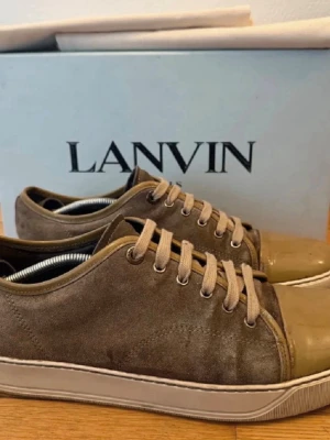 Beige sneakers från Lanvin i mocka - Stilrena sneakers från Lanvin i beige mocka med matchande snörning och gummisula. Skorna har en glansig tå i ljusare beige och klassisk låg siluett. Perfekta för dig som gillar exklusiva och minimalistiska sneakers med premiumkänsla. De är med box. Perfekta till sommaren🔥😎