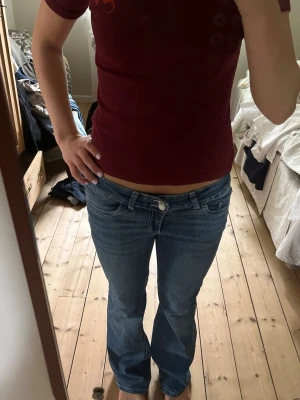 Blå bootcut jeans med broderade fickor - Säljer ett par blå bootcut jeans med låg midja och snygga broderade detaljer på bakfickorna. Jeansen har klassisk femficksdesign och är tillverkade i denim med lätt tvättad look. Perfekta för en avslappnad och trendig stil.
