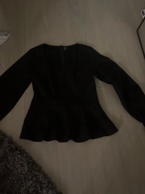 Svart figursydd blus från Shein  - Snygg svart blus från Shein med lång ärm och markerad midja. Blusen har en lätt utsvängd nederdel och en diskret dragkedja bak. Materialet är slätt och ger en stilren look, perfekt för att lyfta din outfit.