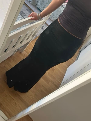 Svart långkjol i stretchigt tyg - Säljer en svart långkjol med figurnära passform. Kjolen är enkel och stilren, tillverkad i ett stretchigt material som sitter snyggt längs kroppen. Perfekt för dig som gillar en klassisk och tidlös look.