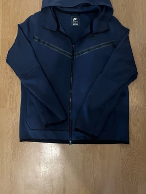 Nike tech fleece - Säljer en snygg och populär Nike Tech Fleece hoodie i mörkblå färg. Perfekt för både vardag, gym och streetwear. Bekväm passform med hög kvalitet och stilren design.  Äkta Nike Mjuk och bekväm Perfekt till alla outfits Storlek: M  Skick: Okej använt skick. Det finns några mindre hål/slitage (se bilder), vilket är inräknat i priset.  