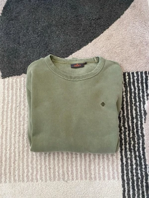 Olivgrön sweatshirt från Morris - Olivgrön sweatshirt från Morris med rund halsringning och diskret logobrodyr på bröstet. Tröjan har ribbade muddar vid ärmslut och nederkant. Perfekt för en avslappnad och stilren look.