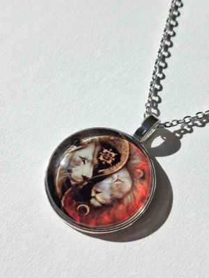 Silverfärgat halsband med lejonmotiv - halsband med runt hänge silverfärgad metall platta i 2D. Hänget har ett konstnärligt motiv yin yang av lejon i rött och guld. Perfekt för dig som gillar djurmotiv och vill sticka ut med din stil.