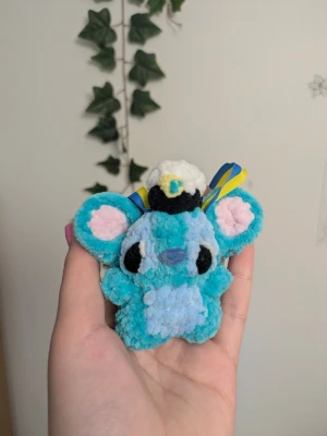 Studenthänge stitch - Söt handgjord blå nalle i garn med stora öron och ljusblå mage. Nallen har en liten studentmössa på huvudet och blågula band, perfekt som dekoration eller present till studenten. Mjuk och fluffig känsla, lätt att hänga upp tack vare banden.