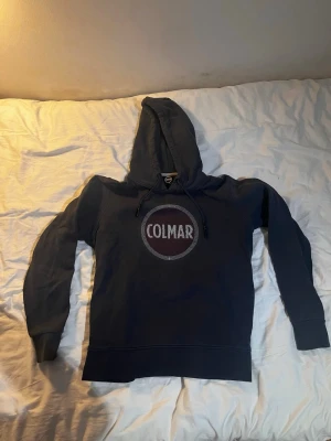 Mörkblå Colmar hoodie  - Säljer en mörkblå hoodie från Colmar i storlek M. Riktigt skönt material och sportig modell som sitter väldigt snyggt på. Stor logga på bröstet.Tröjan är använd men i fint skick. Finns inga hål eller fläckar. Modellen är lite mer slimmad i passformen (italienskt märke).