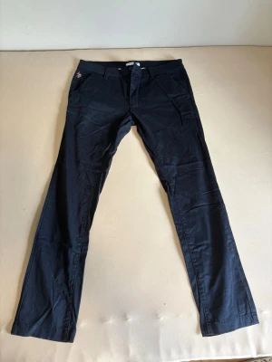 Mörkblå chinos från U.S POLO ASSN - Snygga mörkblå chinos med rak passform och klassisk design. Byxorna har framfickor, bälteshällor och diskreta bakfickor. Tillverkade i ett mjukt bomullsmaterial som ger en skön känsla hela dagen.