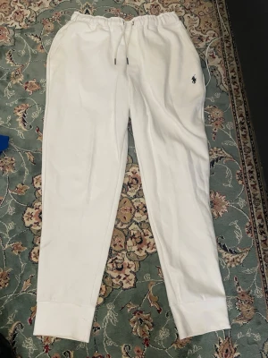 Vita mjukisbyxor från Polo Ralph Lauren - Säljer ett par vita mjukisbyxor från Polo Ralph Lauren med dragsko i midjan och resår vid bensluten. Byxorna har sidofickor och den klassiska lilla loggan broderad på ena benet. Perfekta för chill dagar eller när du vill vara extra bekväm.