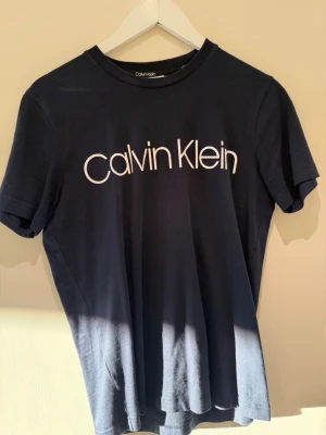 Svart Calvin Klein t-shirt XS - Snygg svart t-shirt från Calvin Klein med klassisk vit logga framtill. T-shirten har rund halsringning och korta ärmar. Perfekt för en stilren och enkel look.