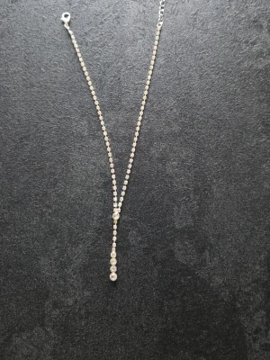 Silverfärgat halsband med gnistrande pärlor - Snyggt halsband i silverfärg med små gnistrande pärlor längs hela kedjan och ett hängsmycke med större, runda pärlor i rad. Perfekt för dig som gillar stilrena och eleganta accessoarer. Materialet ser ut att vara metall med glittrande stenar.