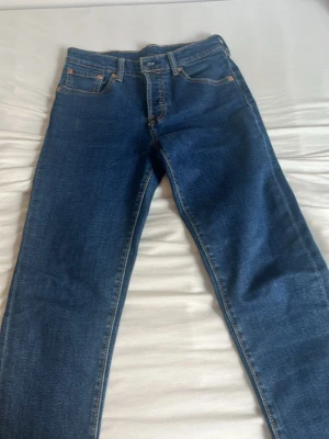 Mörkblå Levi's jeans med raka ben - Säljer ett par klassiska mörkblå jeans från Levi's med raka ben och fem fickor. Jeansen har den ikoniska röda Levi's-lappen på bakfickan och snygga kontrastsömmar. Tillverkade i slitstark denim som passar perfekt till en avslappnad stil. 152cm