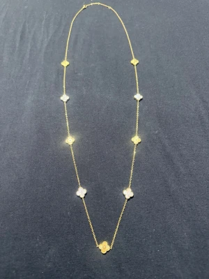 Guldhalsband med klöverhängen - Snyggt halsband i guld med flera små fyrklöverformade hängen längs kedjan. Vissa hängen är i guld och andra i vit pärlemor, vilket ger en lyxig och elegant känsla. Perfekt accessoar för att lyfta vilken outfit som helst.
