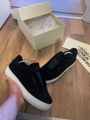 Svarta sneakers från Axel Arigato - Stilrena svarta sneakers från Axel Arigato med ovandel i mocka och vit, chunky gummisula. Diskret logga på sidan och klassisk low-top design. Perfekta för dig som gillar minimalistisk och clean stil. Storlek 40 passar 41