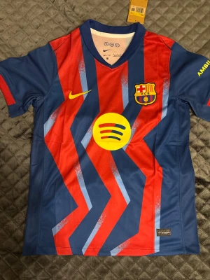 Barcelona matchtröja Nike Dri-FIT - Snygg Barcelona matchtröja från Nike med Dri-FIT material. Tröjan är blå och röd med gula detaljer, klubbmärke och sponsorlogga på bröstet. Perfekt för dig som älskar fotboll och vill bära ditt favoritlag på match eller träning.