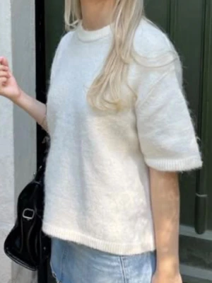 Vit stickad t-shirt med kort ärm - Säljer en enkel och stilren vit stickad t-shirt med korta ärmar och rund hals. Tröjan har en avslappnad passform och ribbade kanter vid ärmslut och nederkant. Perfekt att matcha med jeans eller kjol för en clean look.