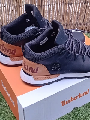 Svarta Timberland sneakers med bruna detaljer - Snygga Timberland sneakers i svart med bruna detaljer och vit sula. Skorna har lågt skaft, rund tå och snörning framtill. Tillverkade i slitstarkt material med mesh vid ankeln för extra komfort. Timberland-logga på sidan och hälen.
