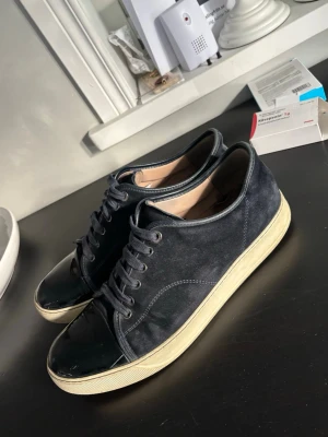 Lanvins stl 45 - Snygga mörkblå sneakers med ovandel i mocka och tåparti i blankt lack. Skorna har vita sulor och klassisk snörning. Perfekta för dig som gillar en stilren och modern look med en twist.